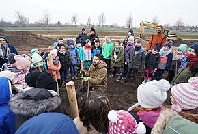 Baumpflanz-Aktion des MIYA e. V.: Menschen (vor allem Kinder) stehen im Kreis um einen Mann, der einen Baum pflanzt