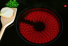 Angeschaltetes Glaskeramikfeld oder Ceranfeld mit Holzlöffel und Zwiebel