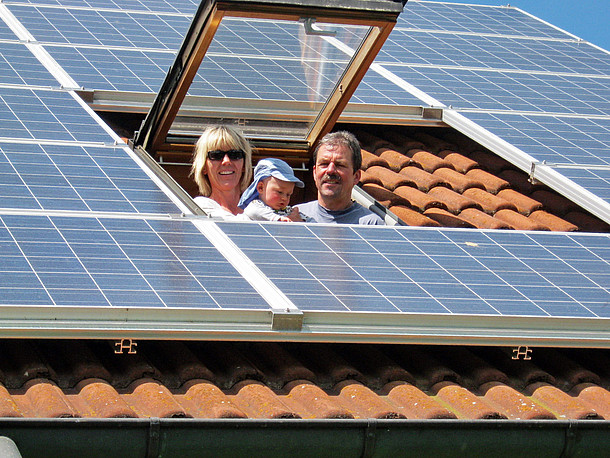 Solarmodule auf einem Dach mit Dachfenster, aus dem Frau, Baby und Mann herausschauen