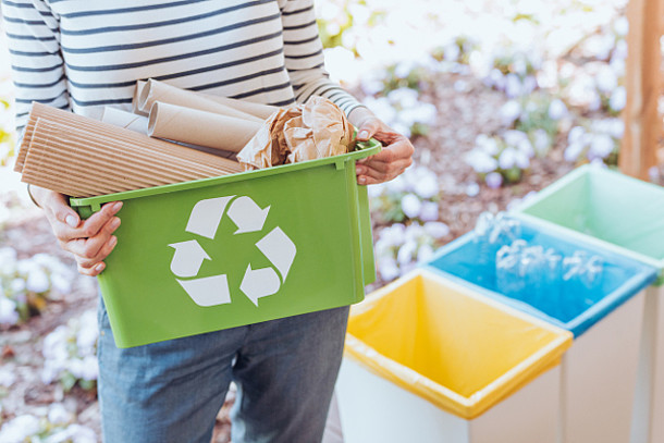 Frau hält einen Recycling-Behälter mit Papier.