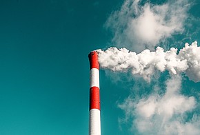 rot-weiß gestreifter Schornstein vor blauem Himmel. Weißer Rauch steigt aus Schornstein auf.