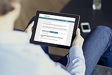 Mann sitzt auf der Couch mit einem Tablet und schaut sich den Fördermittelcheck auf www.co2online.de an.