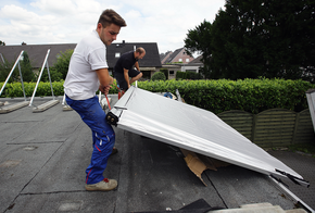 Handwerker tragen Kollektoren aufs Dach.